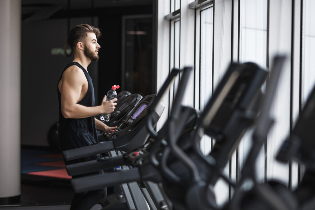 Portrait ofіфвавіфа young sportsman making cardio workout and drinking water in the gym.